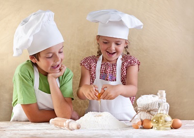 Children in chef's hat and apron baking.