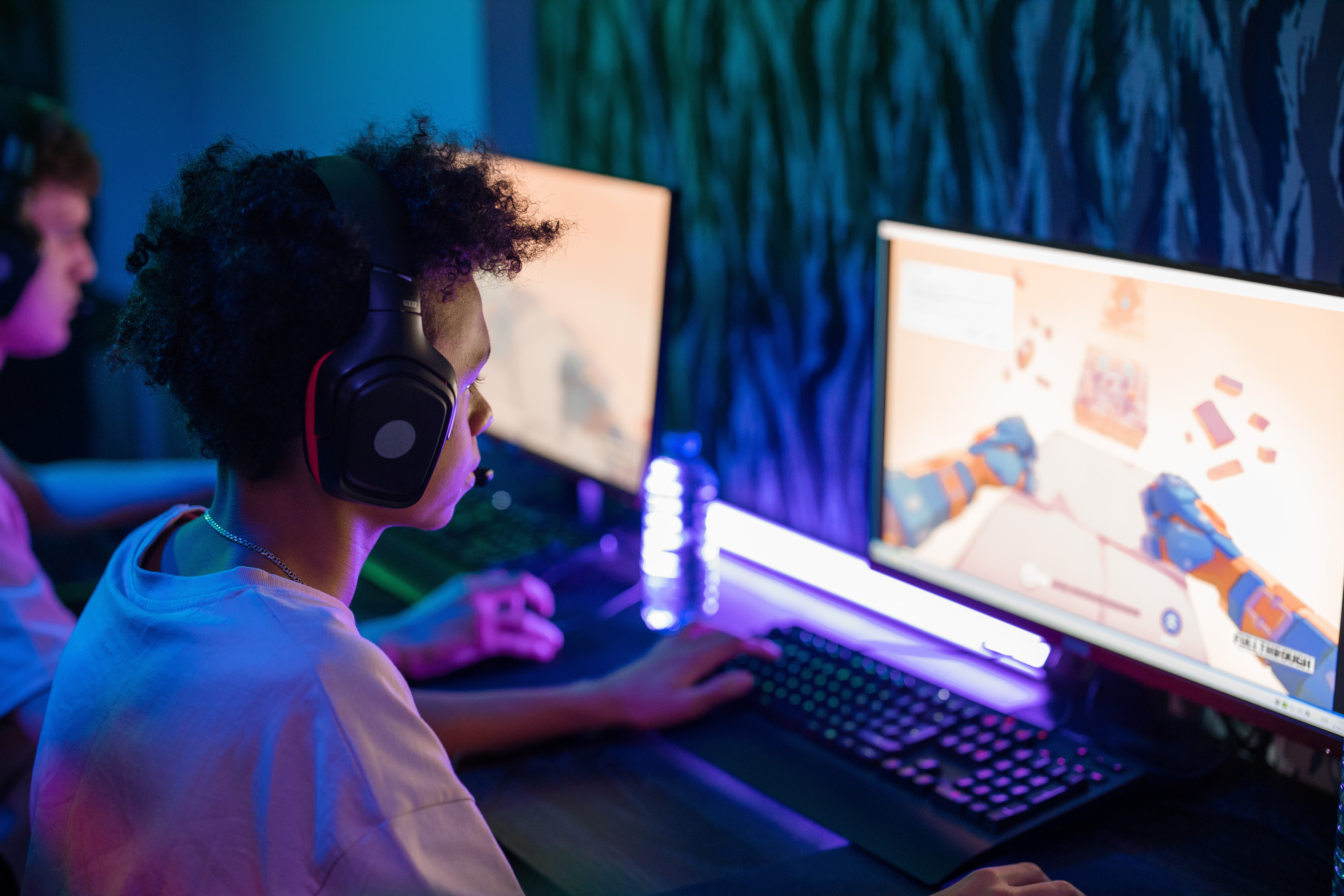 Teens at computer with headphones on playing a video game.