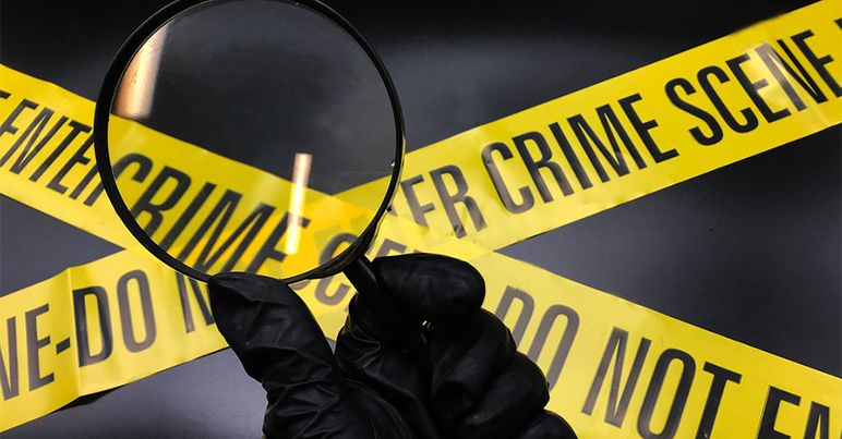 Gloved hand holding a magnifying glass with yellow crime scene tape crossing behind it.