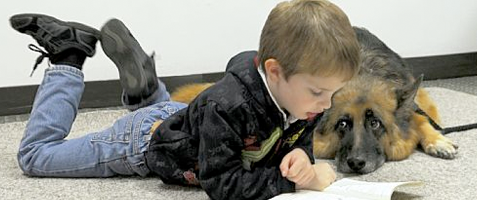 Boy laying on the floor reading to dog.