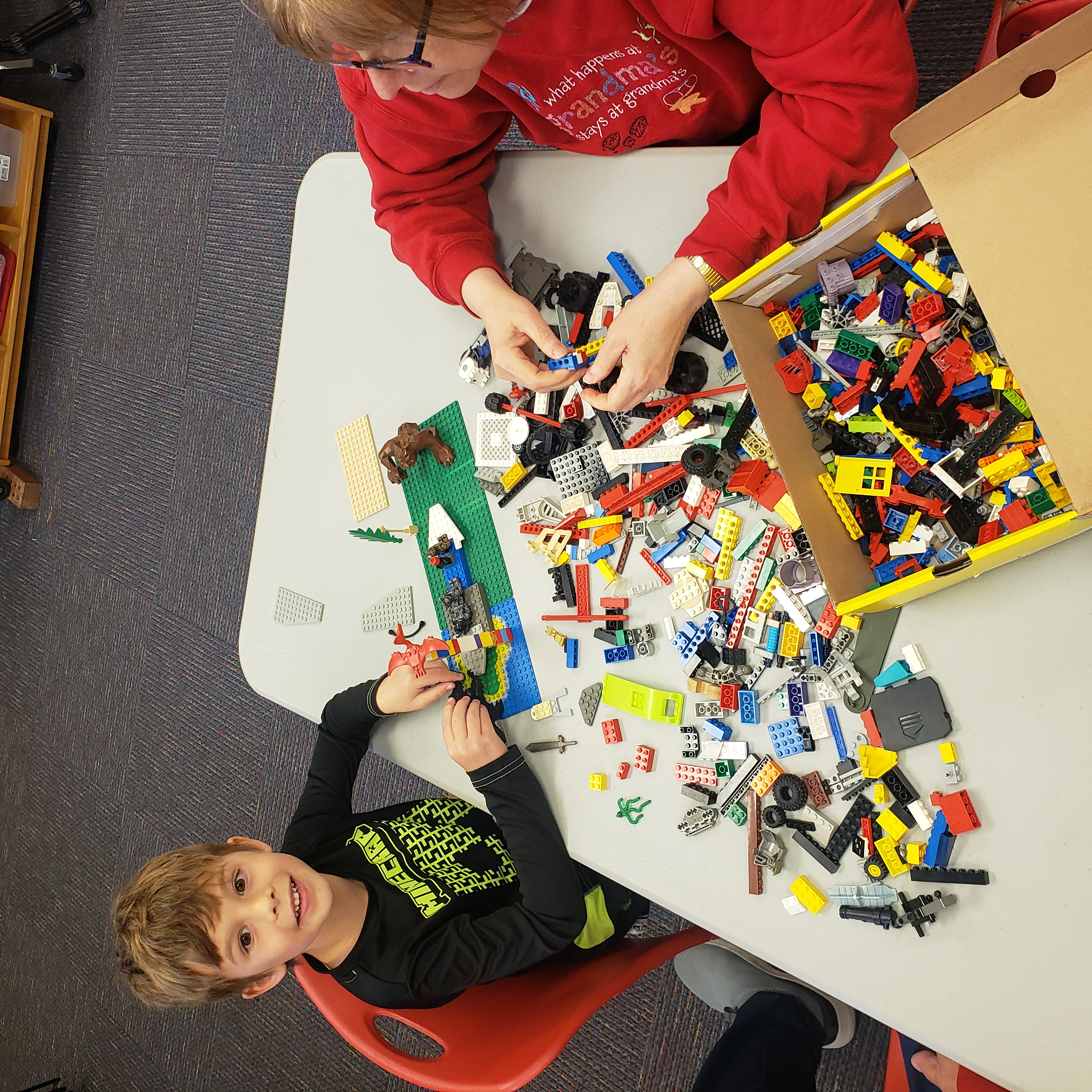 Boy and grandmother with Lego building pieces between them on the table.