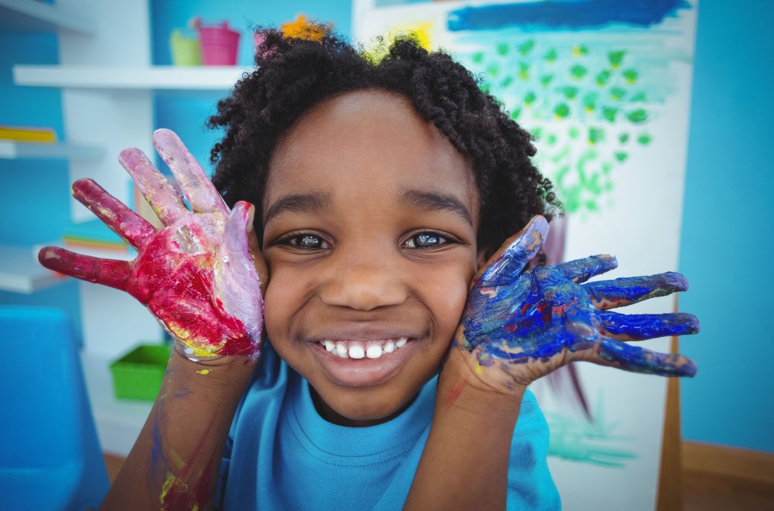 Child holding up hands covered with red and blue paint.