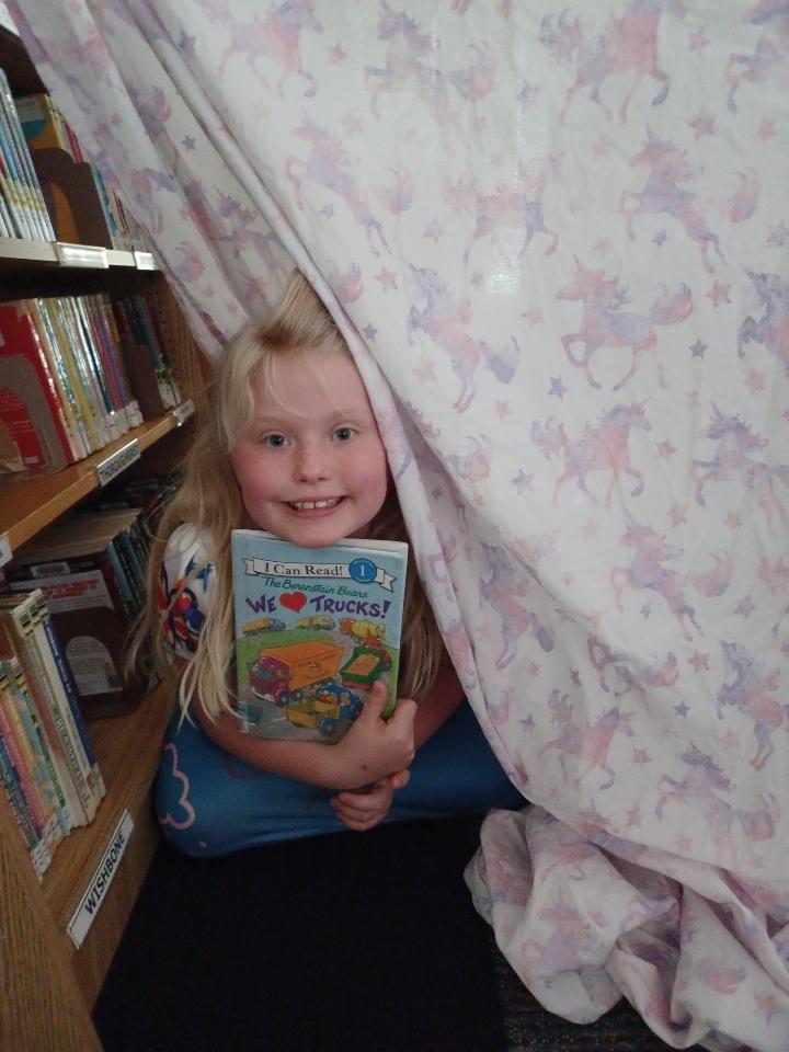 Little girl with blond hair holding a book, peeking out from behind a blanket