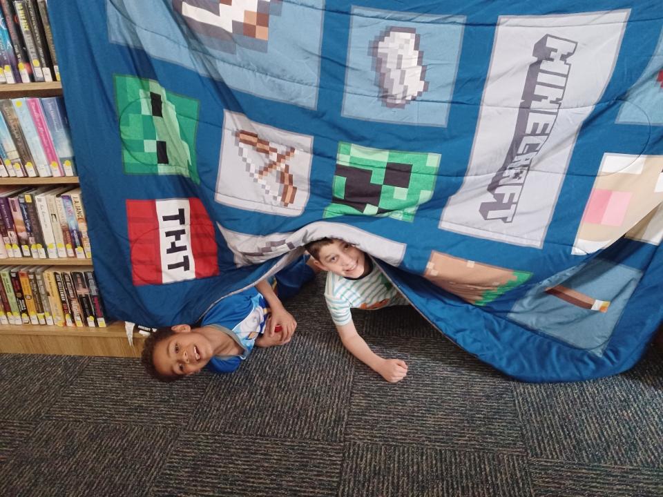 2 boys peeking out from behind colorful quilt