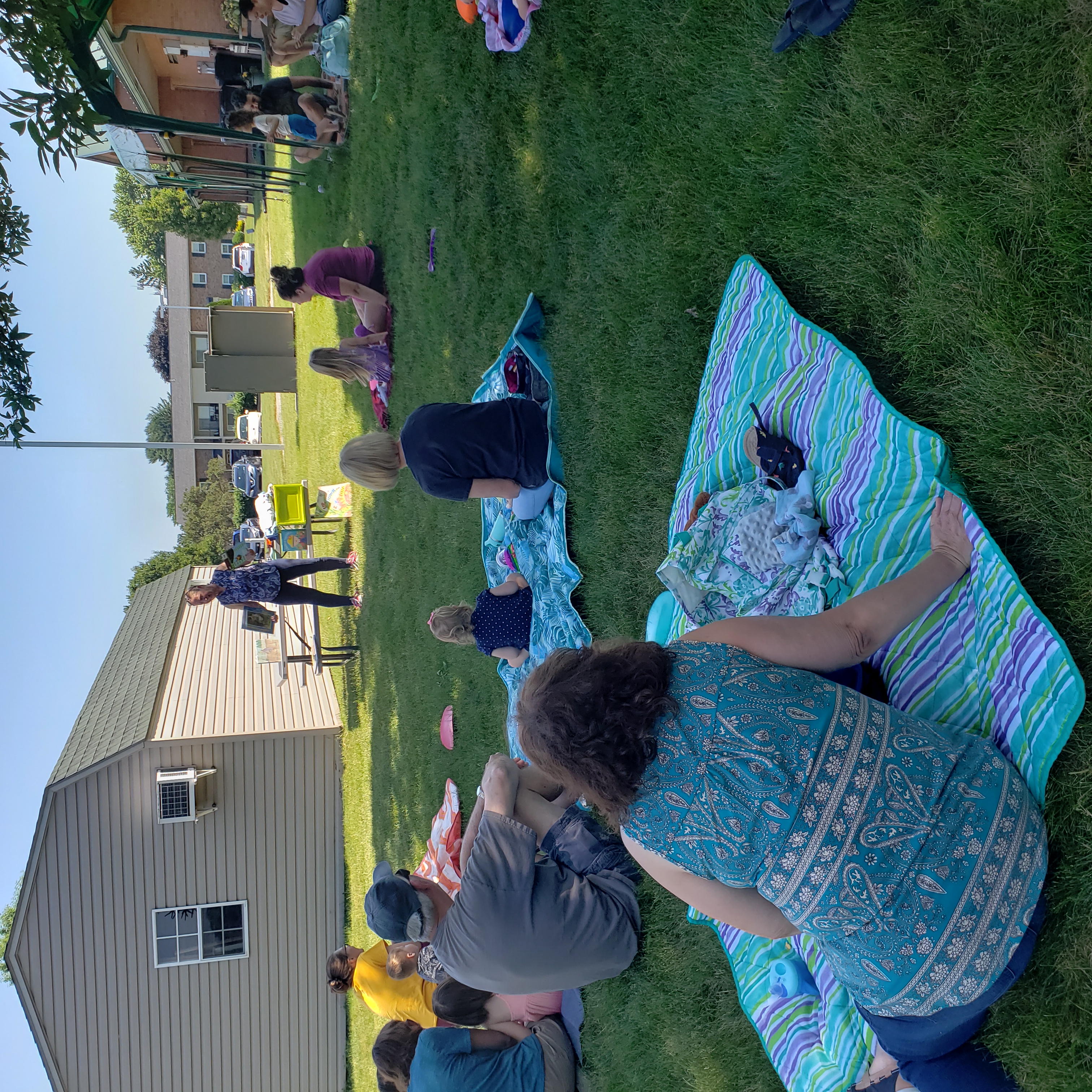 people sitting on blankets on grass while Miss Jan reads stories