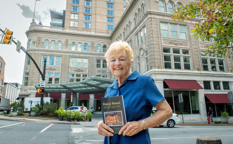 older woman in blue shirt, holding a book, standing in front of iconic building
