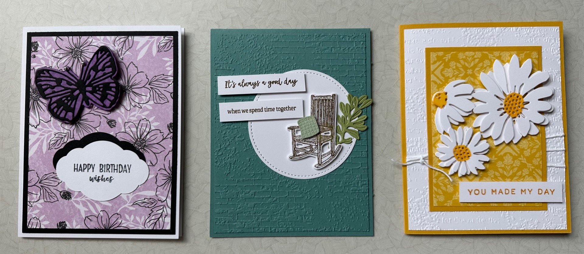 Photo of three cards you can make during class. Left one is purple with a butterfly, the middle is teal with a rocking chair, and the one on the right is yellow with flowers. 