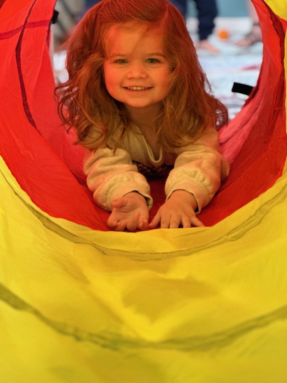 Child playing in a red and yellow tunnel during story time