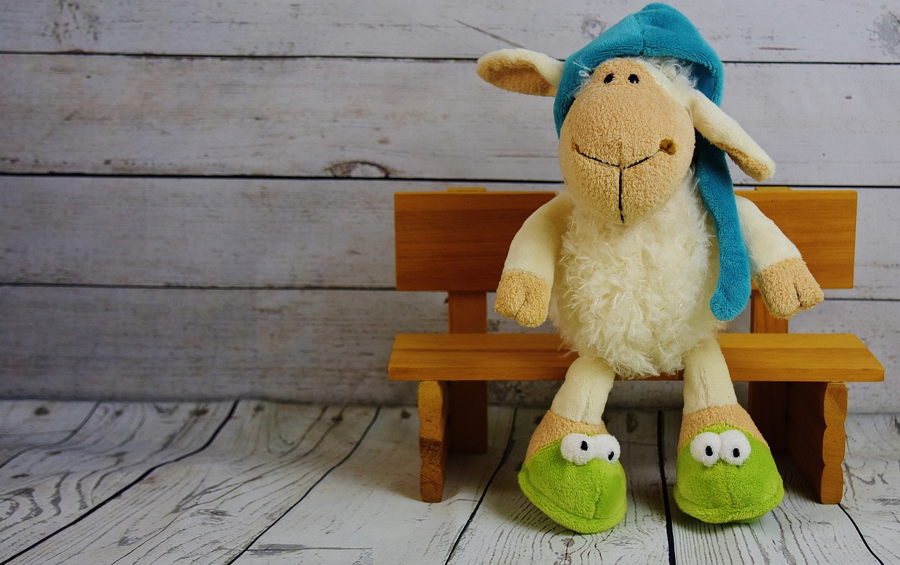 sheep stuffed toy wearing blue hat, green slippers, sitting on a wood bench