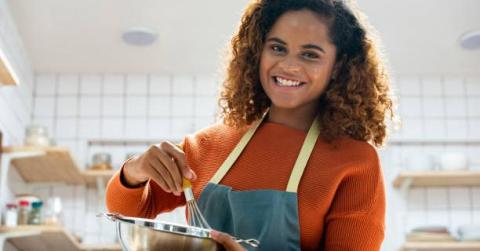 Teen wearing a blue apron stirring something in a bowl using a whisk. 