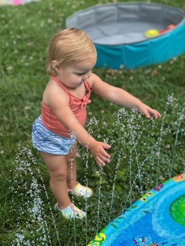 Child playing in sprinkler during water play. 