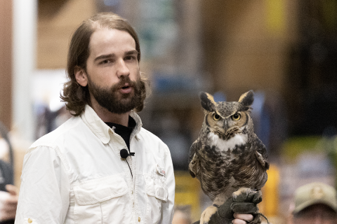 Photo of man in white shirt with beard holding an owl.