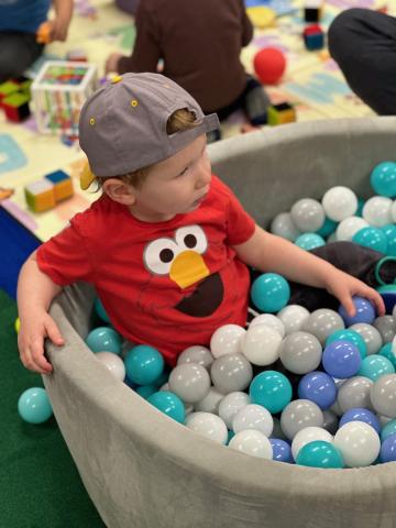 Child playing in ball pit. They are wearing a red shirt and have their hat on backwards.