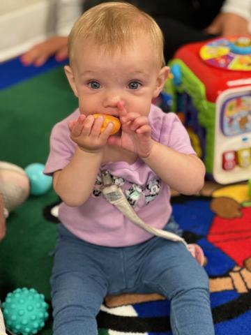 Child in purple shirt and blue pants playing with toy. 