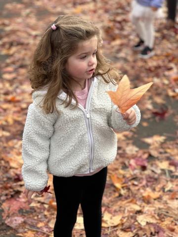 Child in white coat holding leaf