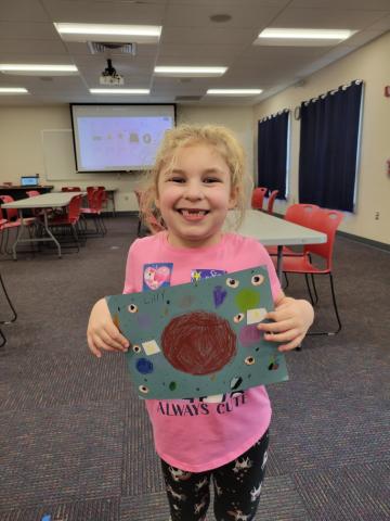 Little girl in pink shirt holding her artwork