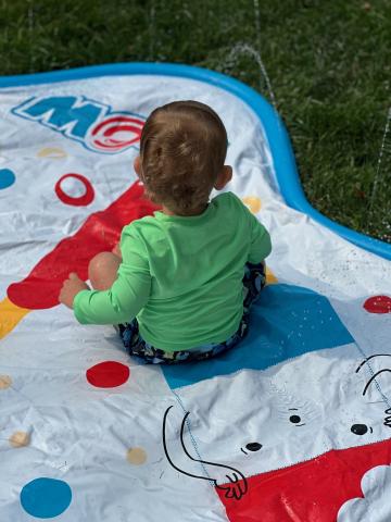 Child with green shirt sitting on white, blue, and red splash mat