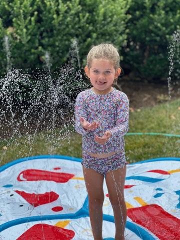 Child playing on red/white and blue sprinkler pad during water play.