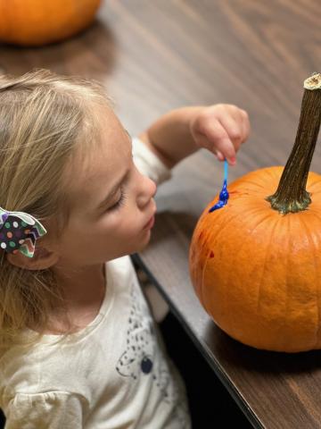 Child in white shirt painting orange pumpkin