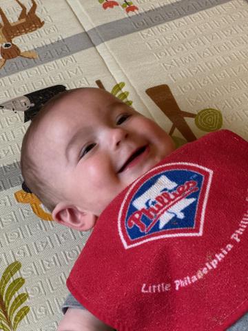 Child wearing Phillies bib smiling on mat