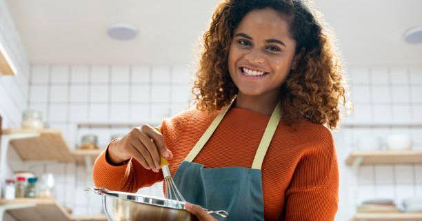 Teen wearing a blue apron stirring something in a bowl using a whisk. 