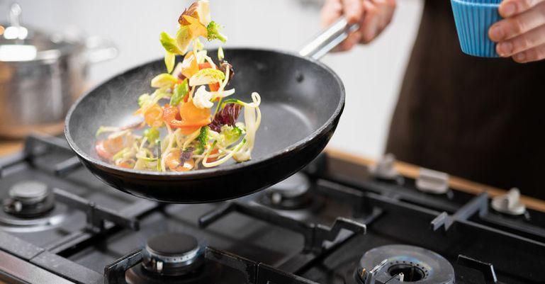 Colorful vegetables being flipped in pan over gas burner.