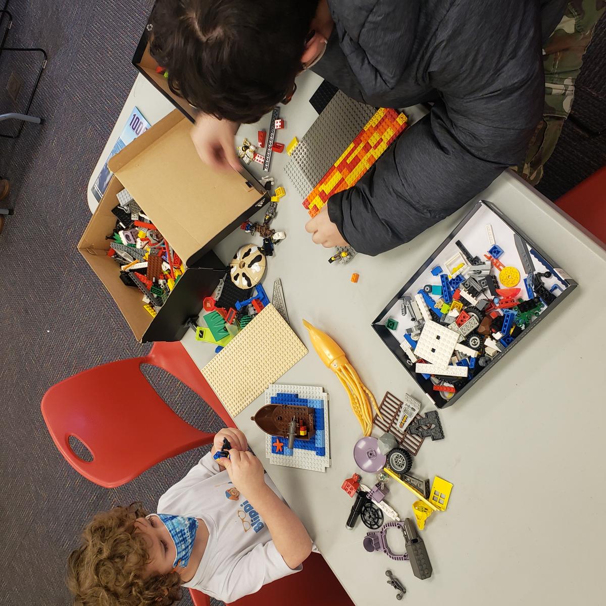 2 children sitting across from each other at a table building with Legos