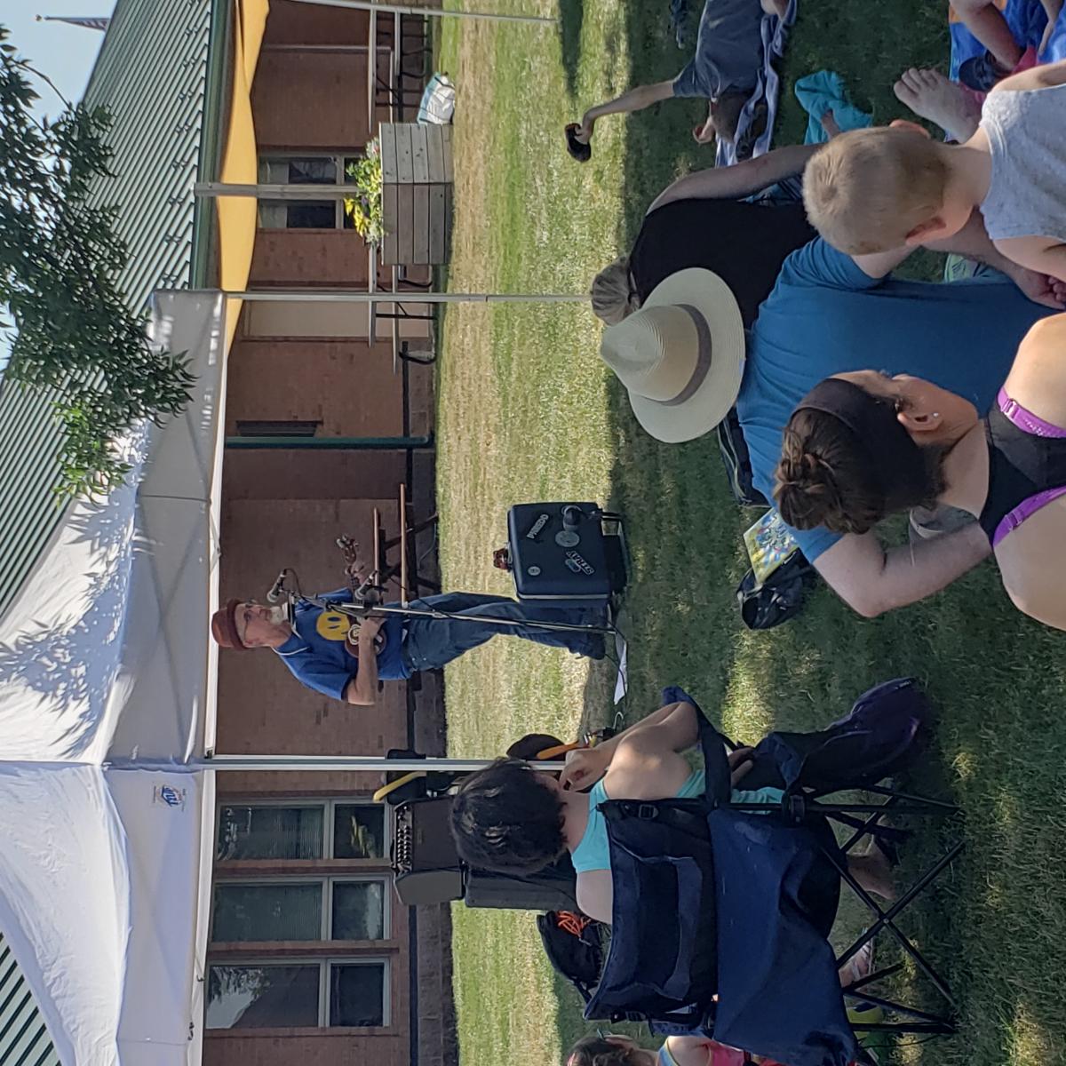 music singing by microphone, people sitting on grass watching