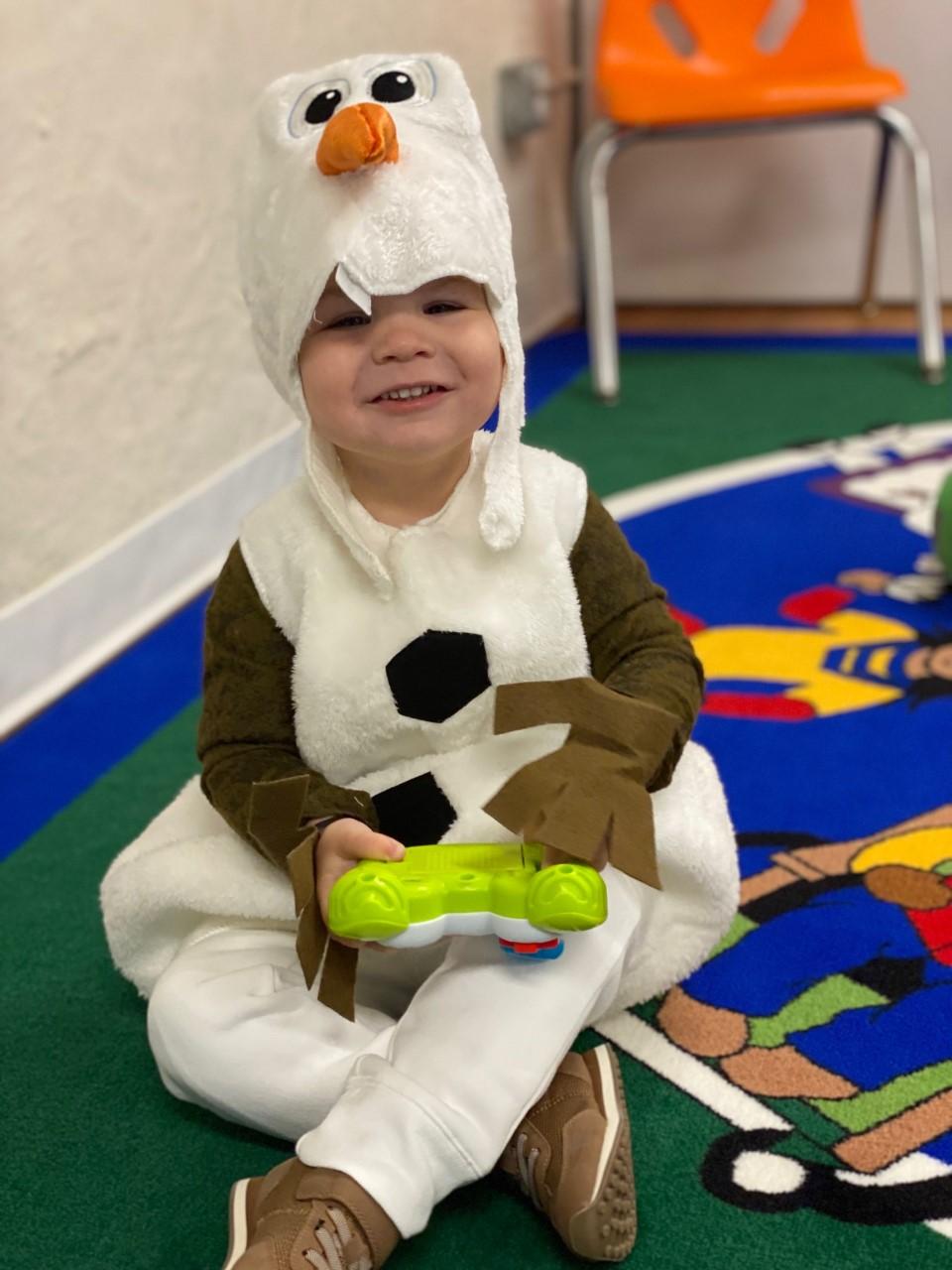 Child wearing white snowman costume and playing with toy during story time 