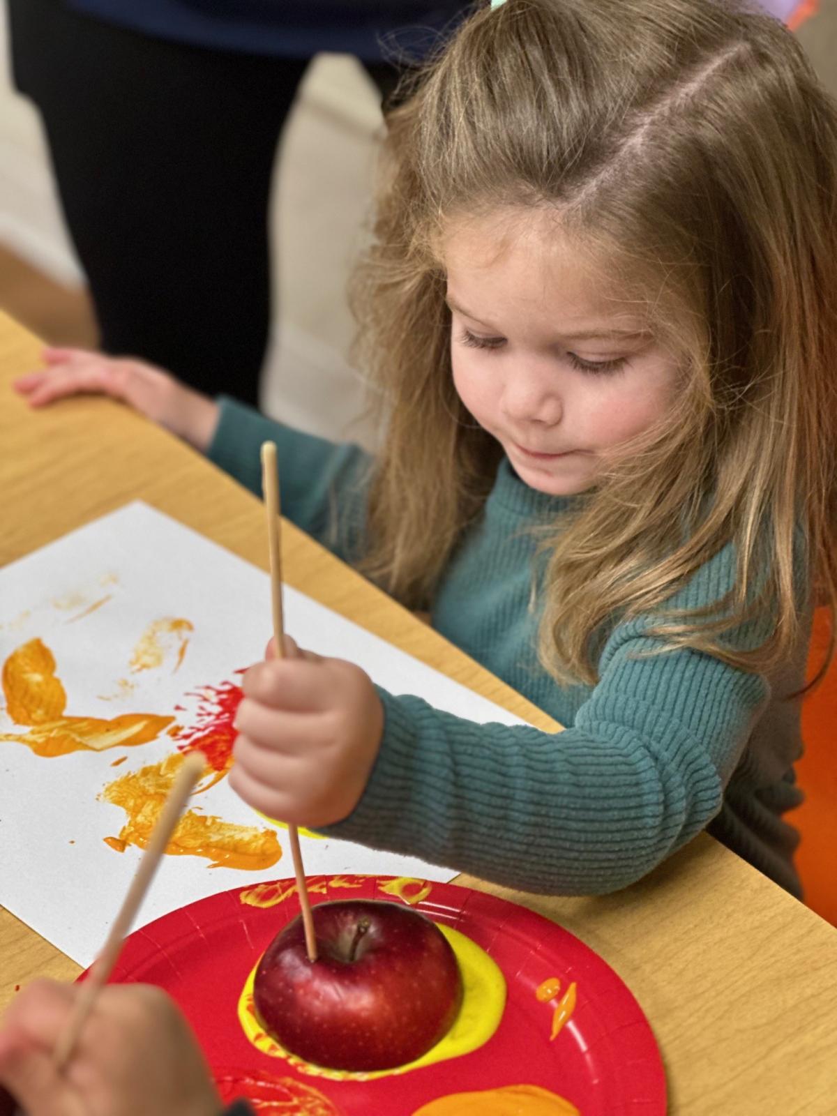 Child wearing green shirt painting with apple