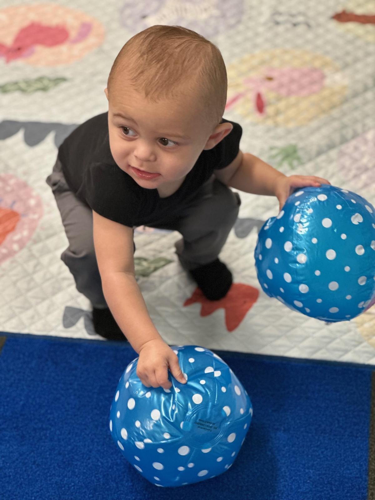 Child playing with two blue balls with white polka dots. 