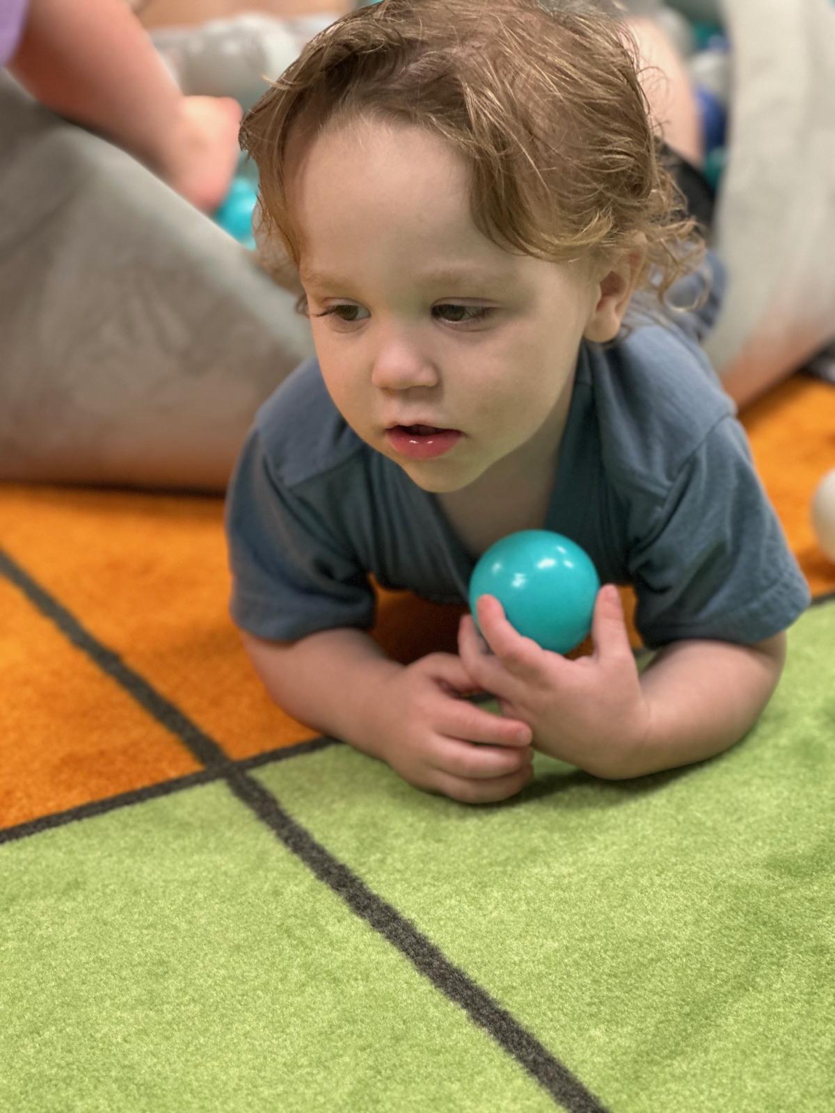 Child playing in ball pit holding teal ball. 