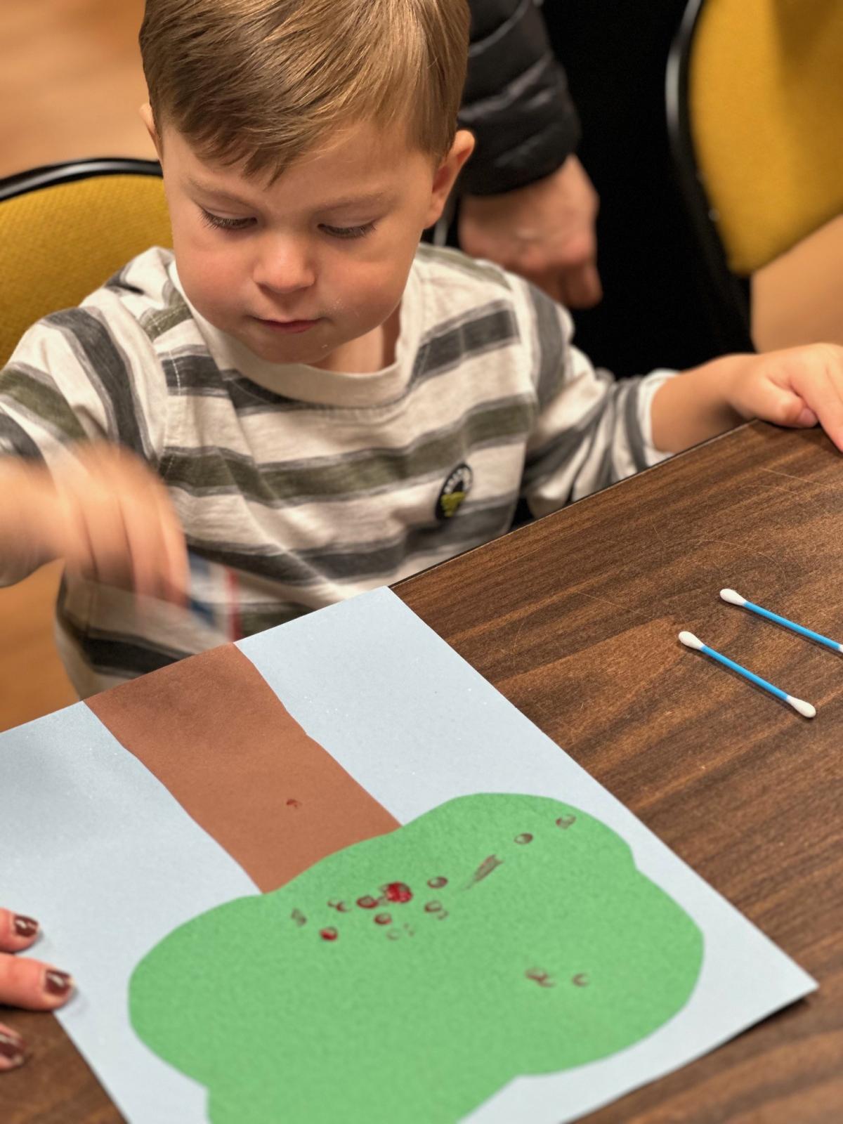 Child using red paint to put apples on their tree