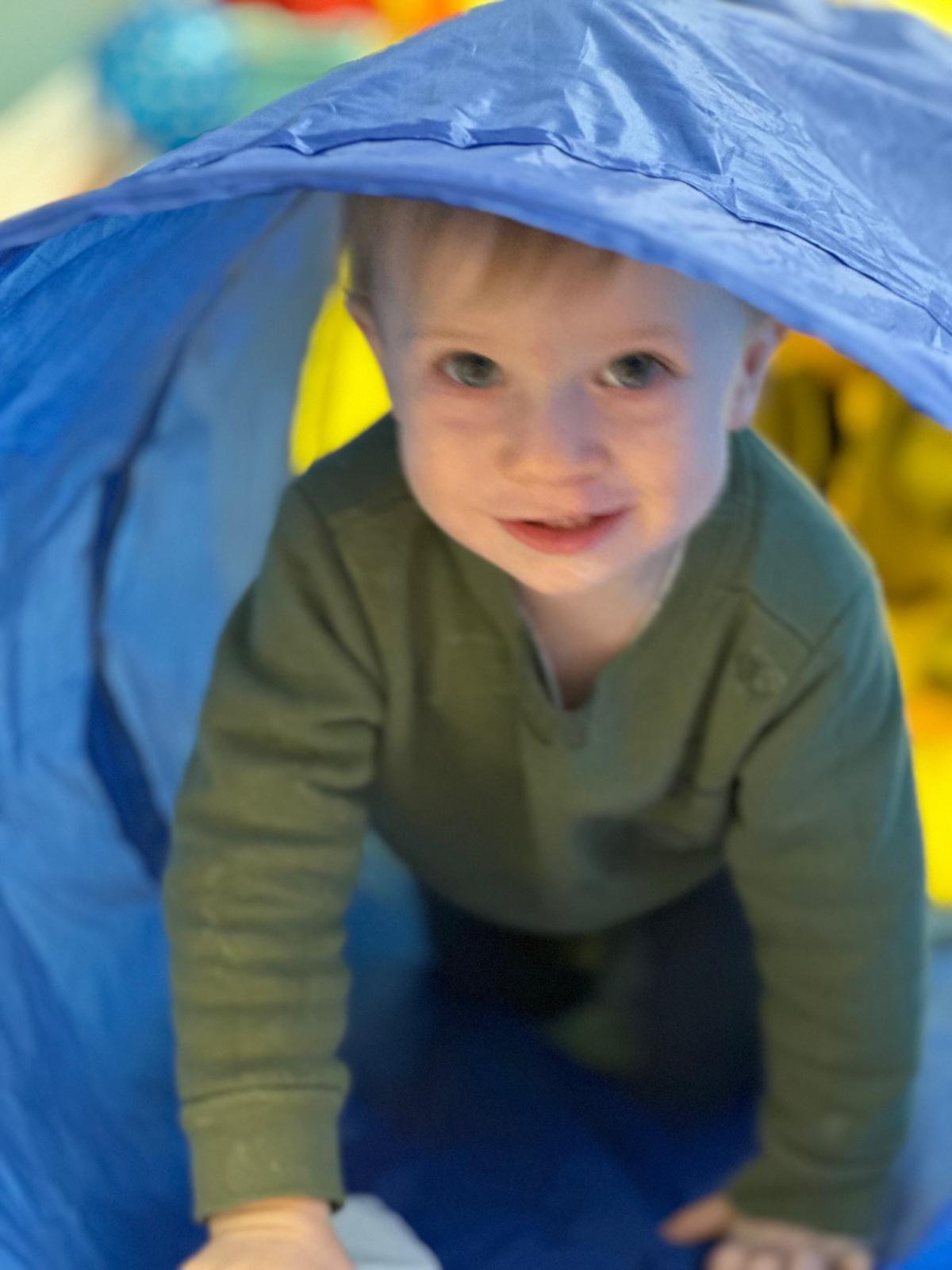 Child wearing green shirt crawling through tunnel