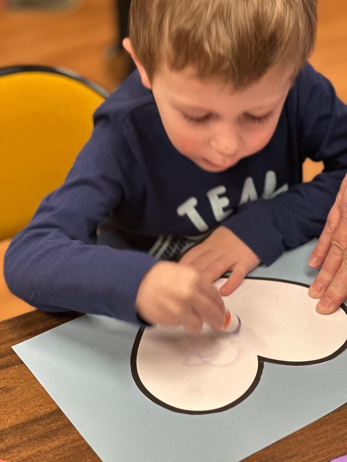 Child in blue sweatshirt working on heart craft 